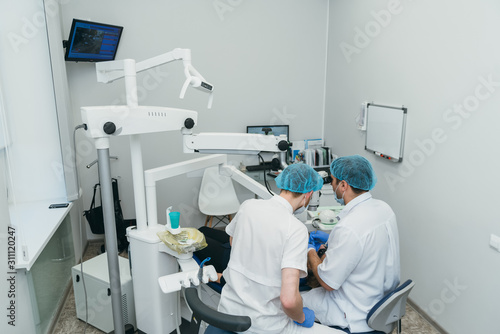 Doctor used microscope. Dentist is treating patient in modern dental office. Operation is carried out using cofferdam. Client is inserted and restored teeth  make denture. Orthodontist and assistant