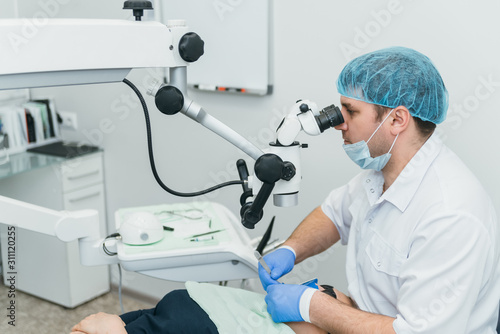 Doctor used microscope. Dentist is treating patient in modern dental office. Operation is carried out using cofferdam. Client is inserted and restored teeth, make denture. Orthodontist and assistant