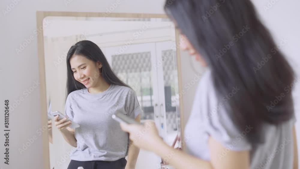 Happy young woman combing her hair while using a smartphone in front of the mirror. Shot in 4k resolution Happy young woman combing her hair while using a smartphone in front of the mirror. Shot in 4k resolution