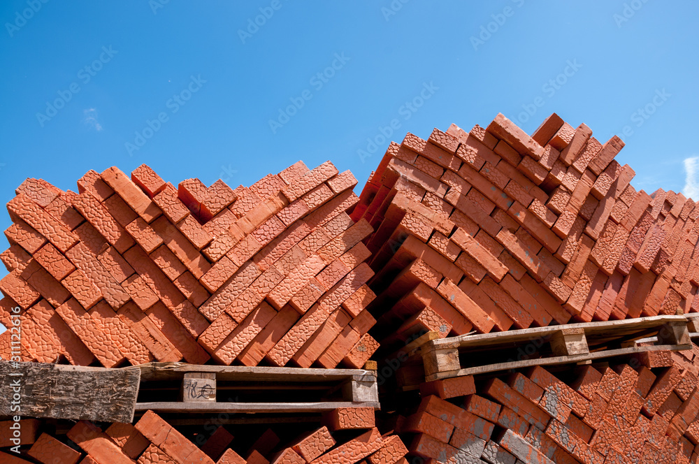 Red bricks stand on pallets on an outdoor construction site in the summer