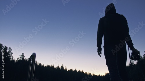 Fototapeta Naklejka Na Ścianę i Meble -  Silhouette traveler photographing scenic view in forest, river. Wood pier. One woman shooting nice dark magic night look. Girl take photo video on camera. Photographer walk with backpack. Outdoor.