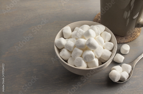 Small white marshmallow in a cream colour bowl, accompanied by a cup of hot beverage.