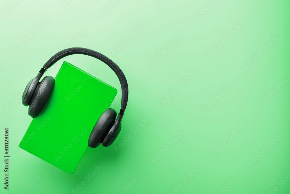 Headphones are worn on a book in a green hardcover on a green background, top view. Headphones are worn on a book in a green hardcover on a green background, top view.