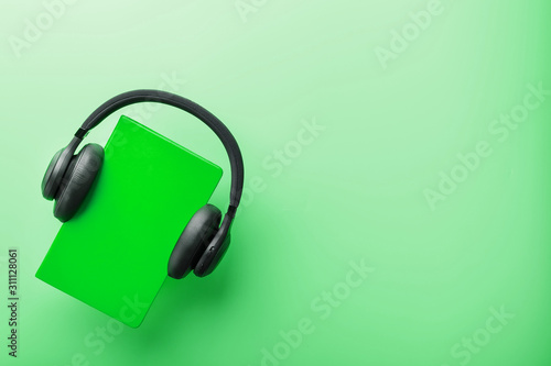 Headphones are worn on a book in a green hardcover on a green background, top view.