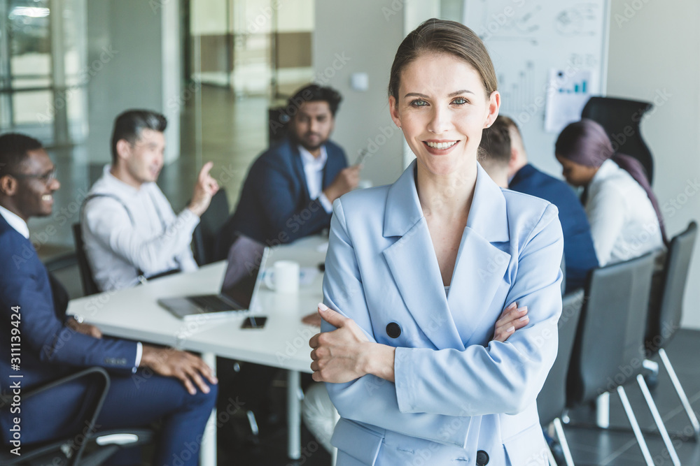 Business woman stands on the background of partners. A team of young businessmen working and communicating together in an office. Corporate businessteam and manager in a meeting Business woman stands on the background of partners. A team of young businessmen working and communicating together in an office. Corporate businessteam and manager in a meeting