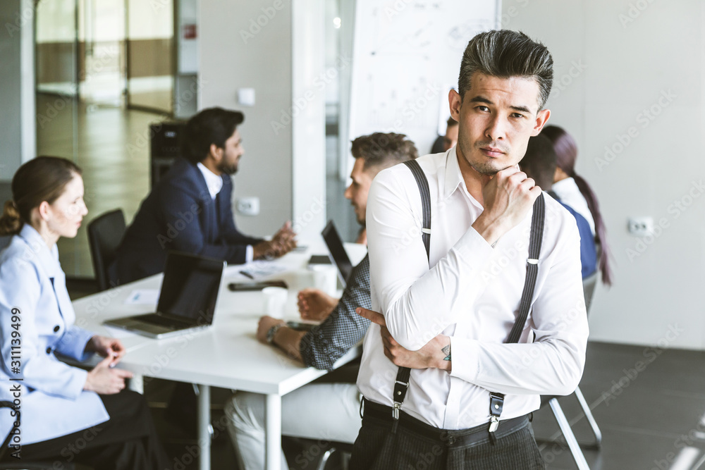 Business man stands on the background of partners. A team of young businessmen working and communicating together in an office. Corporate businessteam and manager in a meeting. Business man stands on the background of partners. A team of young businessmen working and communicating together in an office. Corporate businessteam and manager in a meeting.