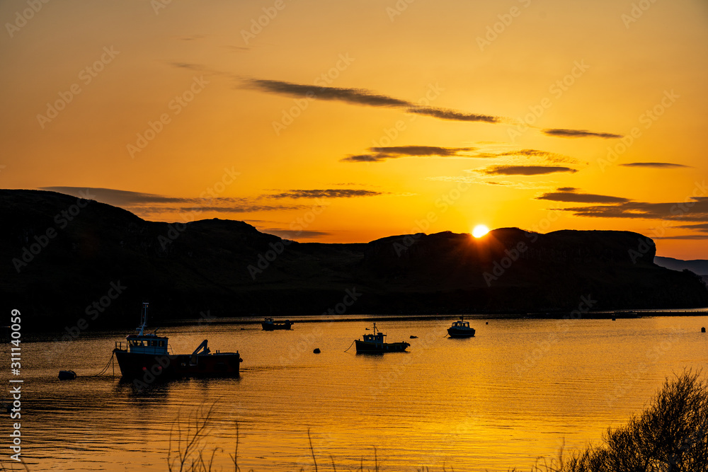 Boats in Portree bay during sunrise with purple and orange colors with hills on both sides on the Isle of Skye