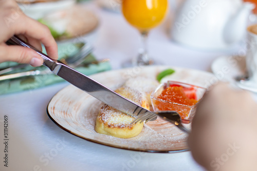 Cheesecakes, baked polpettine di ricotta on a plate with jam and strawberries. On the table is a cup of coffee, a glass of orange juice, a fork and a knife in hand photo
