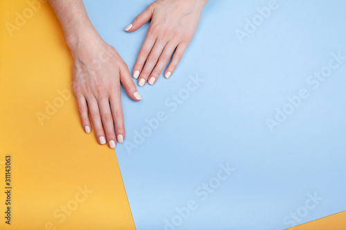 Beautiful female hands with a classic matte manicure on a blue-yellow background. Place for your text.