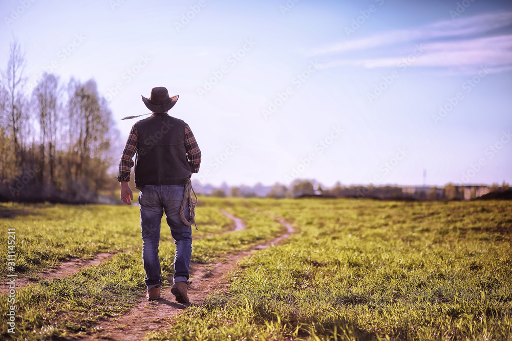 Cowboy standing in a field at sunset