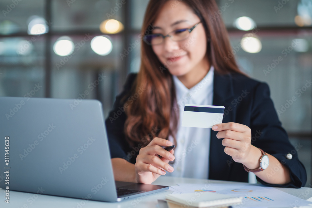 An asian businesswoman holding credit cards while using laptop computer in office An asian businesswoman holding credit cards while using laptop computer in office