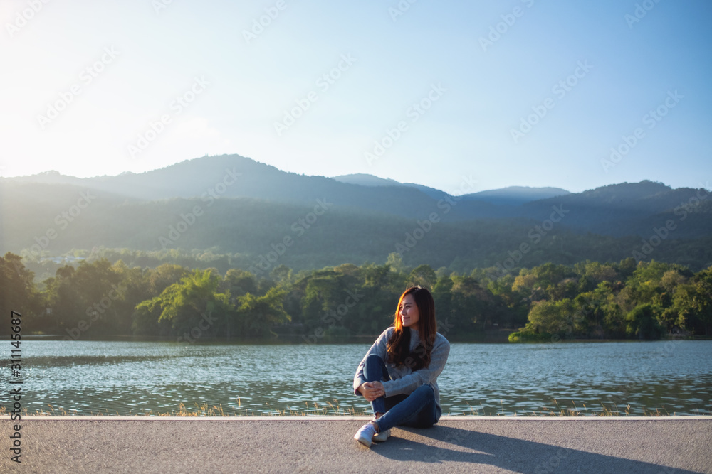 Portrait image of a beautiful asian woman sitting in front of the lake and mountains before sunset