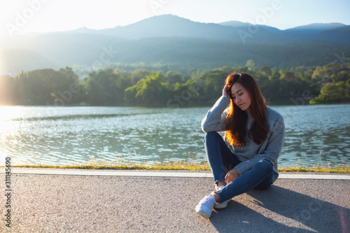 Portrait image of a sad woman sitting in front of the lake and mountains before sunset