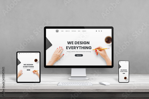 Web design studio with multiple devices on office desk. Concept of responsive, flat web page design. Modern devices with thin edges on wooden desk photo