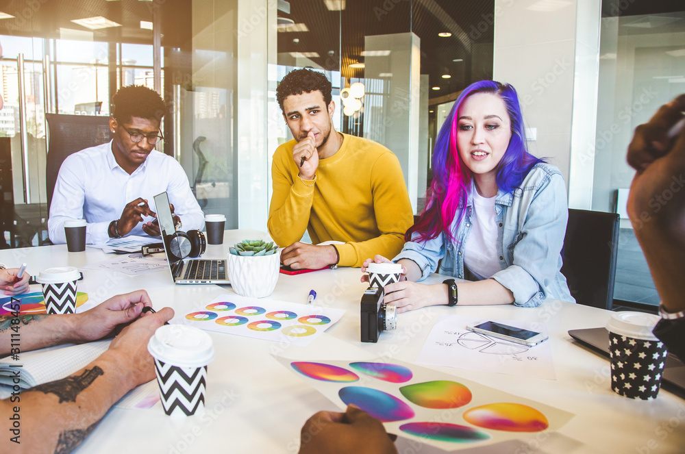 Fototapeta premium Group of multi ethnic executives discussing during a meeting. Business man and woman sitting around table at office and smiling. A team of young creative designers
