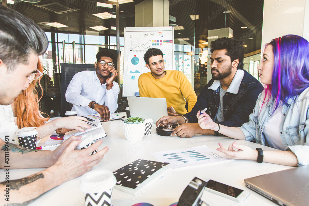 Fototapeta premium Group of multi ethnic executives discussing during a meeting. Business man and woman sitting around table at office and smiling. A team of young creative designers