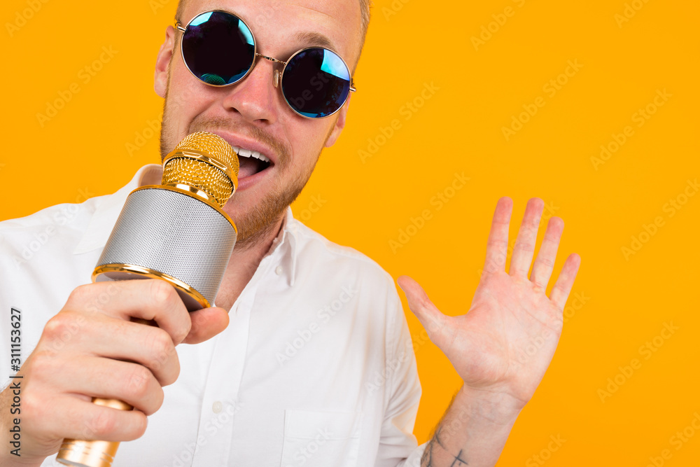 Beautiful caucasian man with glasses sings songs in karaoke with microphone isolated on yellow background Beautiful caucasian man with glasses sings songs in karaoke with microphone isolated on yellow background