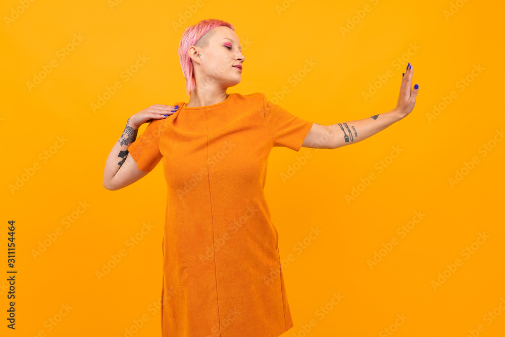 Unusual pretty woman with short pink hair and tattoo smiles isolated on orange background Unusual pretty woman with short pink hair and tattoo smiles isolated on orange background