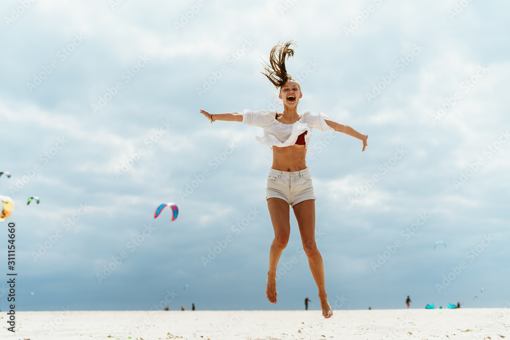 Obraz premium the girl bounced high spreading her arms apart, screaming, opening her mouth, her tail flew up from the hair from the wind up, behind the ocean, sky and kites fly