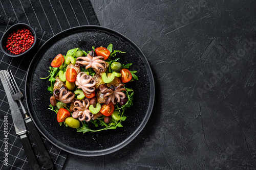 Salad with grilled octopus, potatoes, arugula, tomatoes and olives. Black background. Top view. Space for text