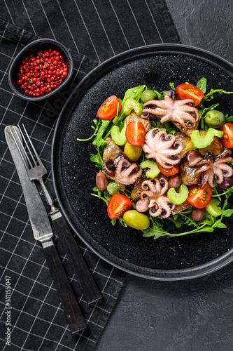 Homemade salad with octopus and potatoes, arugula, tomatoes and olives. Black background. Top view