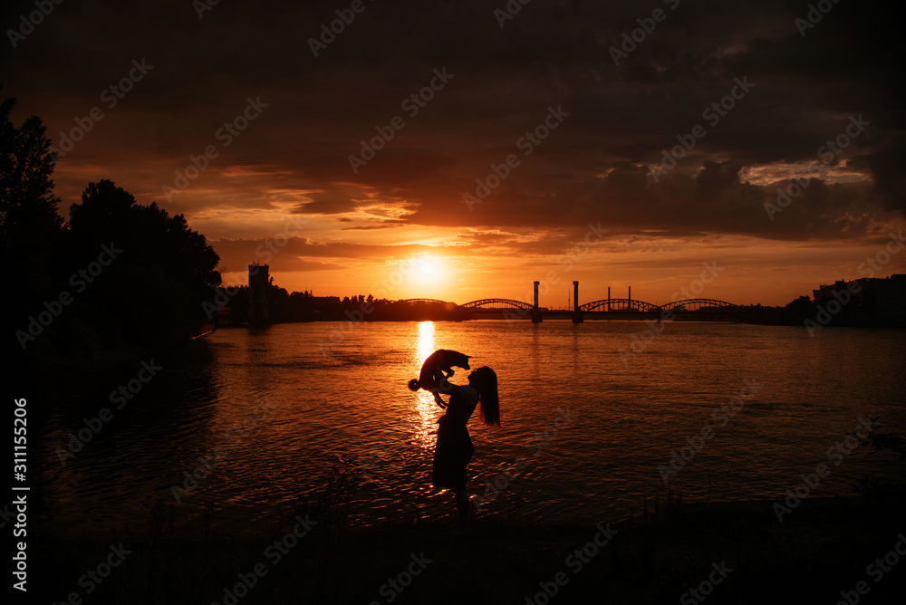 owner holding up a dog by the river a sunset