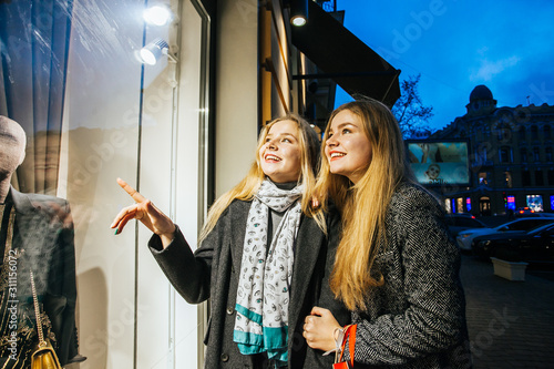 Two women walking past a shop window and looking in. They are shopping during the sales.