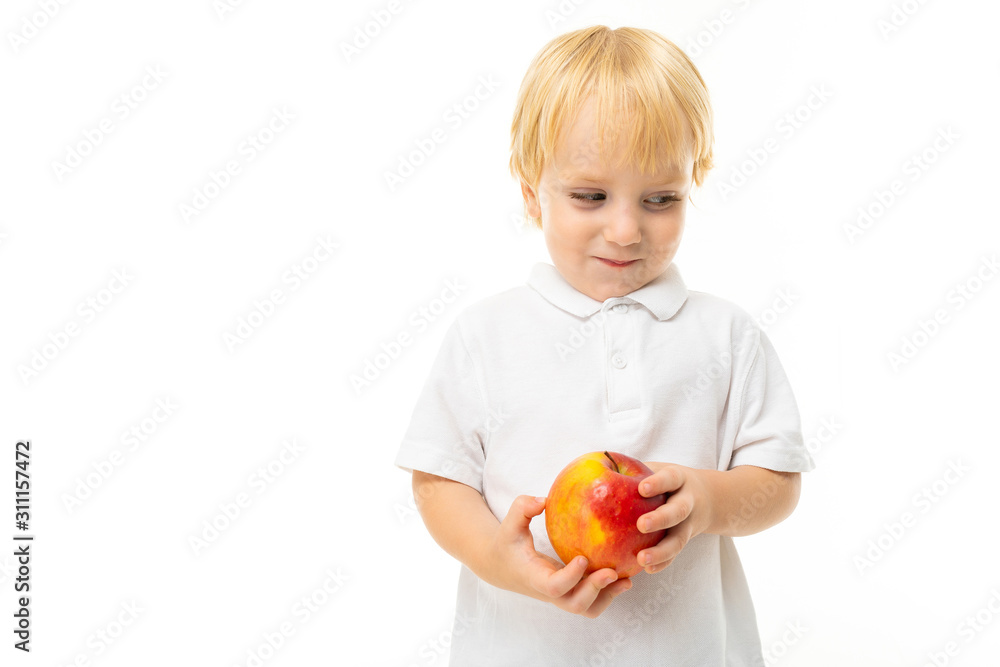 modest charming blonde child dressed in a white T-shirt with an apple in his hand on a white background with copy space modest charming blonde child dressed in a white T-shirt with an apple in his hand on a white background with copy space