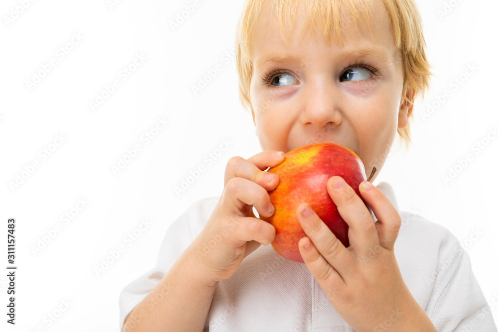 modest charming blonde child dressed in a white T-shirt eats an apple on a white background with copy space modest charming blonde child dressed in a white T-shirt eats an apple on a white background with copy space