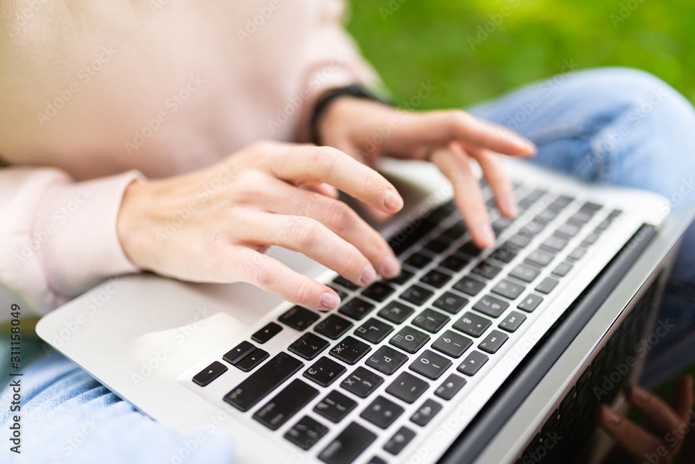 Naklejka premium girl typing on laptop keyboard with mockup sitting on grass in park