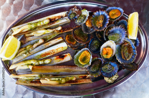 Grilled limpets served with lemon.Razor shells or navajas and lapas grelhadas on a metal plate.Traditional dish of Portugal and a typical snack of the Canary Islands.Seafood concept.Selective focus. photo