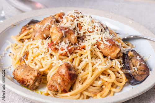 Spaghetti with homemade sausages and eggplant sprinkled with grated cheese in a plate close-up, top view - traditional Italian pasta