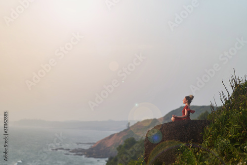 Young girl practices yoga in a red dress on a mountain in India