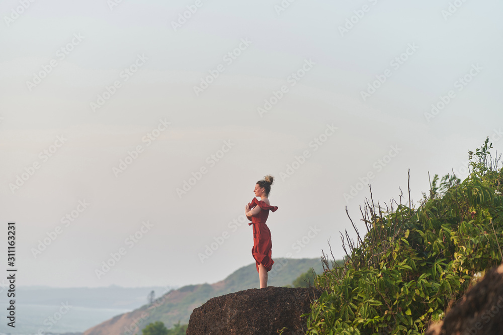 Young girl practices yoga in a red dress on a mountain in India