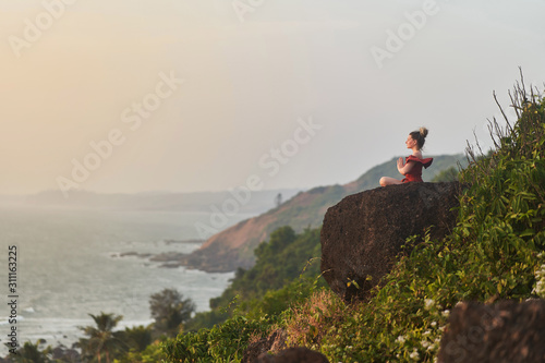 Young girl practices yoga in a red dress on a mountain in India