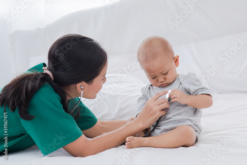 Asian toddler girl get sick examine by pediatrician doctor woman green uniform hold stethoscope, mother or nurse monitoring heart pulse rate adorable infant on bed in clinic, baby health care concept