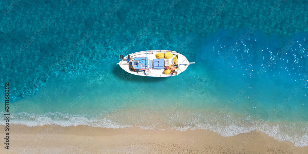 Aerial drone top down ultra wide photo of traditional wooden fishing boat docked in turquoise super paradise beach of Mykonos island, Cyclades, Greece