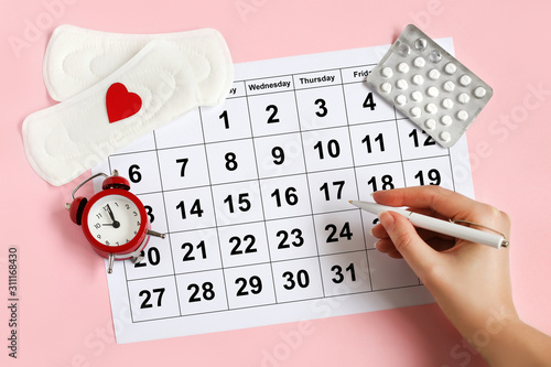 Menstruation calendar with pads, alarm clock, hormonal contraceptive pills. Female's menstrual cycle concept. Menstrual retardation concept photo