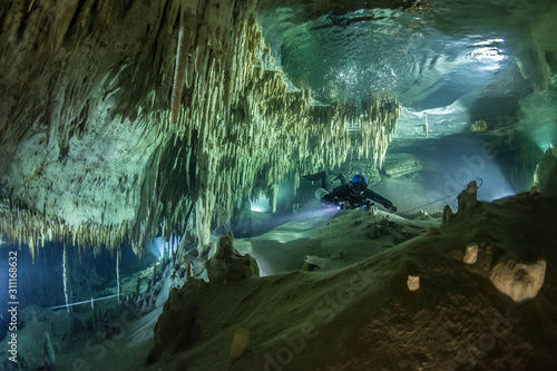 A cave diver swims in the Hulo cenote (Mexico), illuminated by the AMG's underwater light. Karst cave, formed stalactites and stalagmites are visible. photo