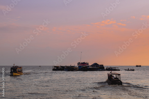 Boats bringing tourists to a floating restaurant on the Tonle Sap Lake in Cambodia during beautiful pink Sunset