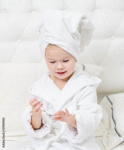 little cute girl painting her nails on the bed in the bedroom in a towel and Bathrobe