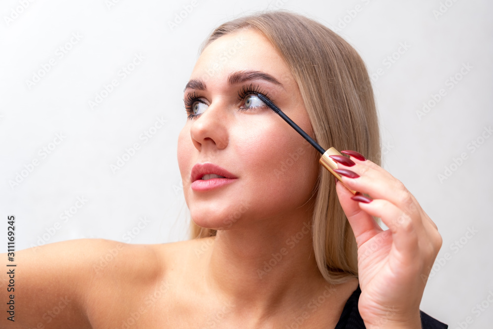 Fototapeta premium Beauty portrait of girl with perfect nude make-up. Painting eyelashes with mascara. Turned aside. Beauty salon. Head and shoulders, studio, indoors.