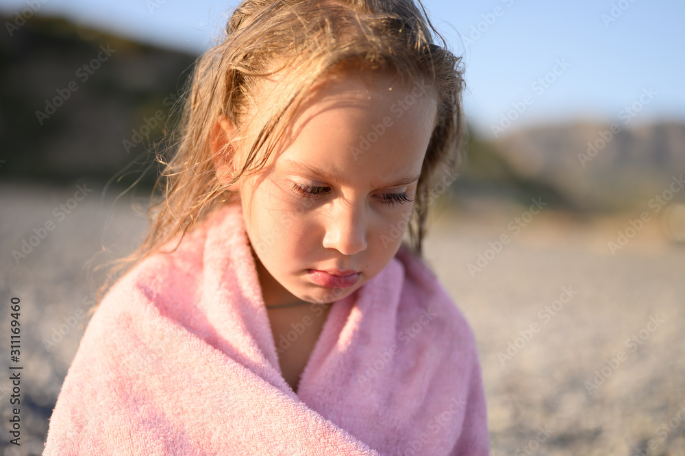 sad six year old little girl resting on the sea beach after swimming