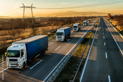 High speed Lorry trucks in line as a caravan or convoy on a country highway under a beautiful sunset sky © Ivan