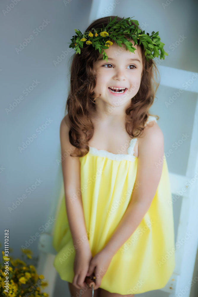 Beautiful girl with curly hair and a wreath on the head in a yellow dress. Beautiful girl with curly hair and a wreath on the head in a yellow dress.