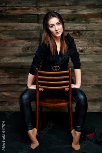 The concept of a glamorous portrait. Portrait of a pretty brunette girl in a black fashion suit on a stylish background in the original interior. Sits on a chair in various poses.