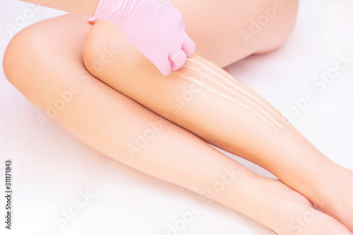 Beautician depilating young womans legs with liquid sugar in spa center. depilation of legs with shugaring paste