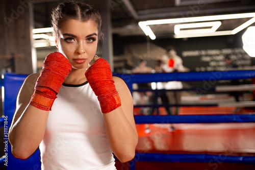 young caucasian MMA girl in sports uniform ready to fight in boxing ring, red bandages on her fists, combat readiness of muscular sportive female