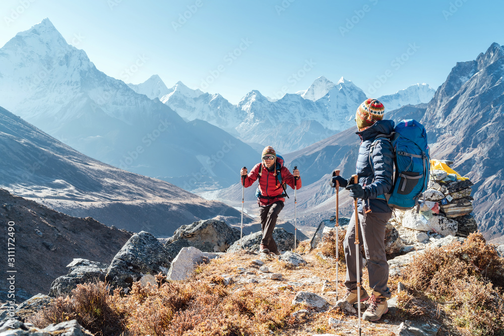 Couple following Everest Base Camp trekking route near Dughla 4620m. Backpackers carrying Backpacks and using trekking poles and enjoying valley view with Ama Dablam 6812m peak