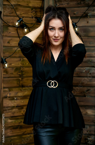 The concept of a glamorous portrait. Portrait of a pretty brunette girl in a black fashion suit on a stylish background in the original interior. Stands in front of the camera in various poses.